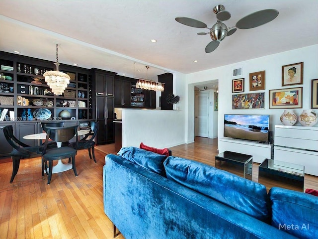 living room featuring visible vents, light wood-style flooring, and ceiling fan with notable chandelier