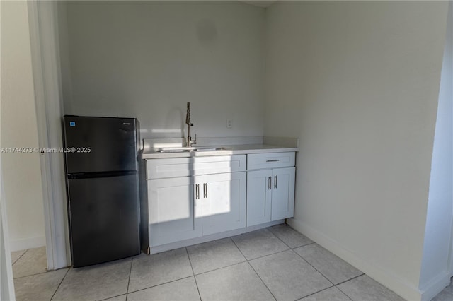 kitchen with black refrigerator, sink, white cabinetry, and light tile patterned flooring