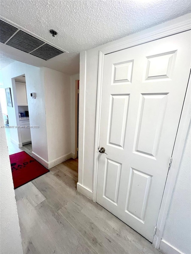 hall with a textured ceiling and light wood-type flooring