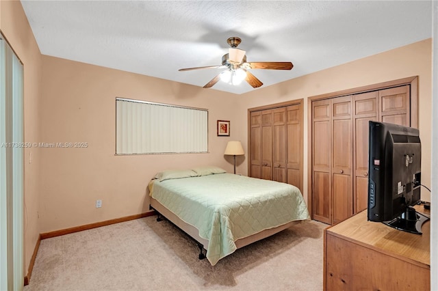 bedroom featuring ceiling fan, light carpet, and two closets