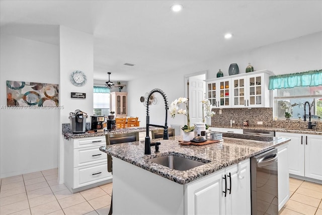 kitchen featuring dark stone countertops, a sink, a kitchen island with sink, and white cabinets