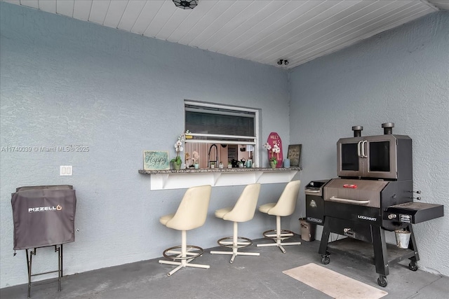 bar featuring concrete flooring, a textured wall, and a dry bar