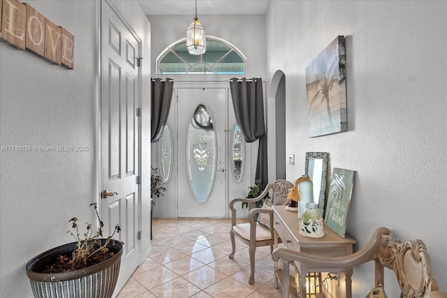 foyer entrance with arched walkways, light tile patterned flooring, and a textured wall