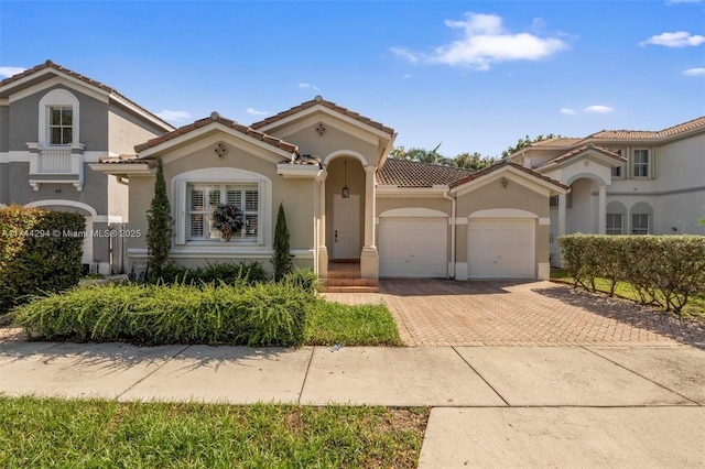 mediterranean / spanish home with a tile roof, a garage, decorative driveway, and stucco siding