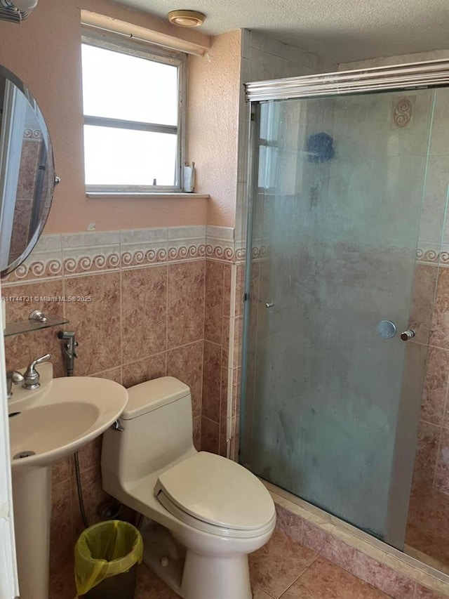 bathroom featuring tile patterned flooring, tile walls, a textured ceiling, a shower with shower door, and toilet