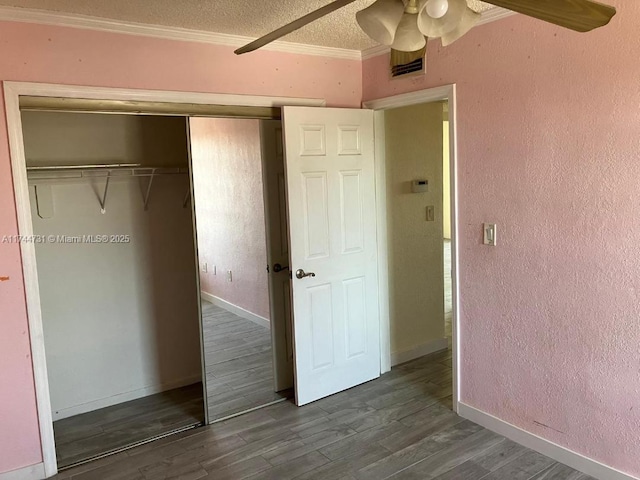 unfurnished bedroom with ornamental molding, ceiling fan, dark wood-type flooring, a textured ceiling, and a closet