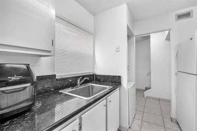 kitchen featuring visible vents, white cabinets, freestanding refrigerator, a sink, and light tile patterned flooring