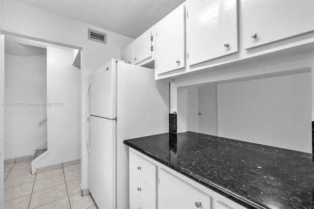 kitchen featuring visible vents, freestanding refrigerator, white cabinets, a textured ceiling, and dark stone countertops