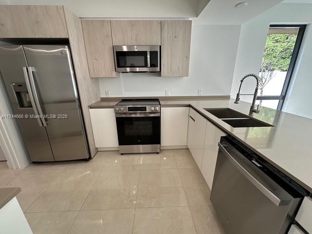 kitchen featuring light brown cabinetry, sink, stainless steel appliances, and light tile patterned flooring