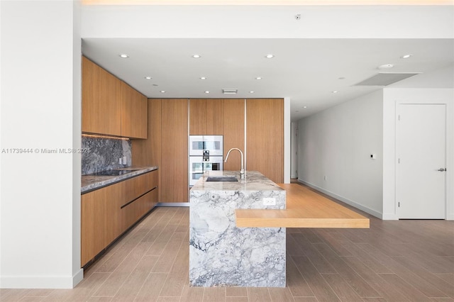 kitchen with tasteful backsplash, sink, light hardwood / wood-style flooring, and a spacious island