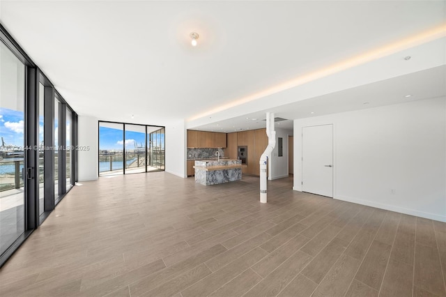 unfurnished living room featuring expansive windows, a water view, and light hardwood / wood-style floors