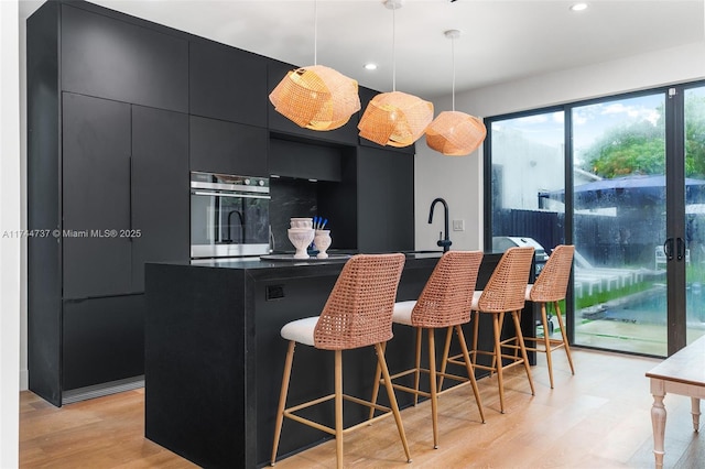 kitchen with a breakfast bar area, decorative light fixtures, a kitchen island, oven, and light hardwood / wood-style floors