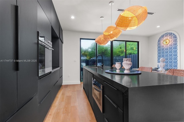 kitchen featuring decorative light fixtures, sink, stainless steel fridge, wall oven, and light wood-type flooring