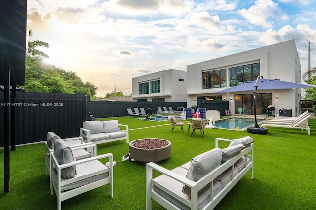 back house at dusk with a pool with hot tub, a yard, and an outdoor living space with a fire pit