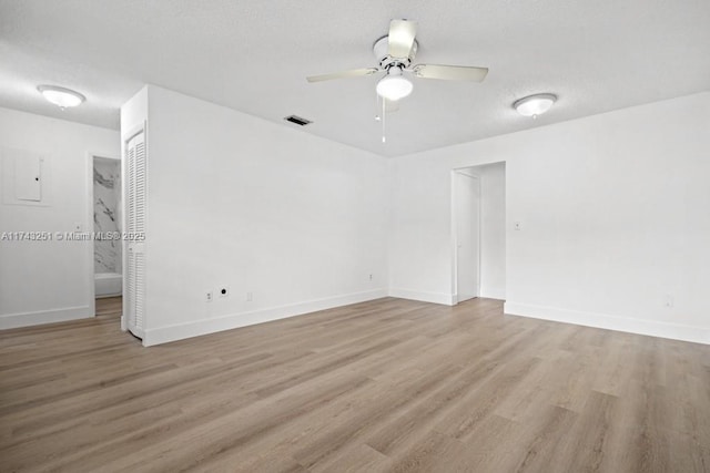 empty room featuring a textured ceiling, light hardwood / wood-style floors, ceiling fan, and electric panel