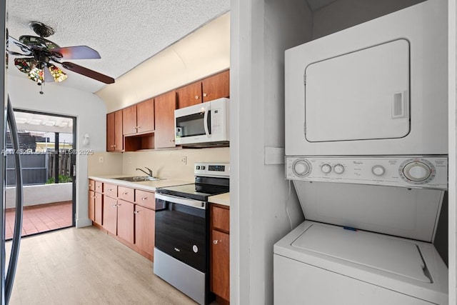 kitchen featuring stacked washer / dryer, sink, ceiling fan, light wood-type flooring, and electric stove