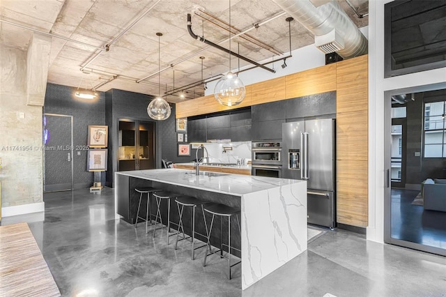 kitchen with appliances with stainless steel finishes, sink, a breakfast bar area, hanging light fixtures, and light stone countertops