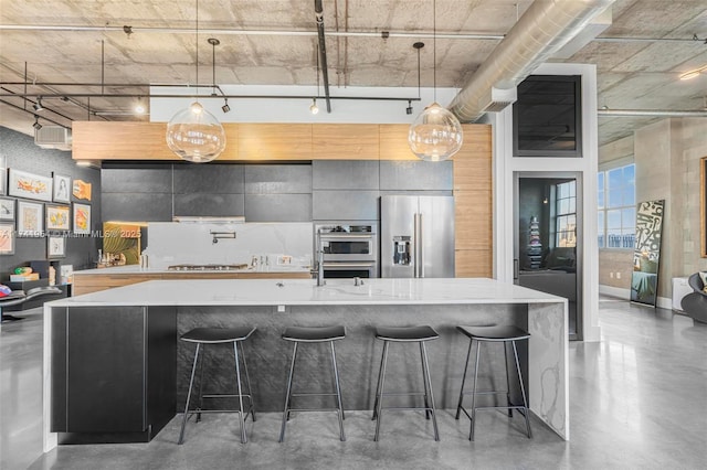 kitchen featuring a breakfast bar, appliances with stainless steel finishes, hanging light fixtures, concrete flooring, and track lighting