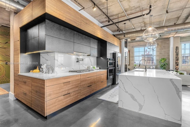 kitchen with decorative light fixtures, light stone countertops, a large island with sink, and appliances with stainless steel finishes