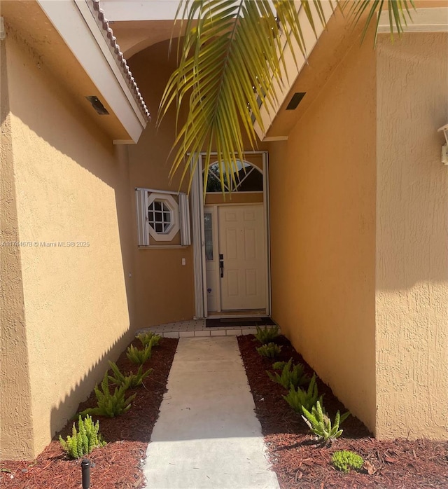 property entrance with visible vents and stucco siding