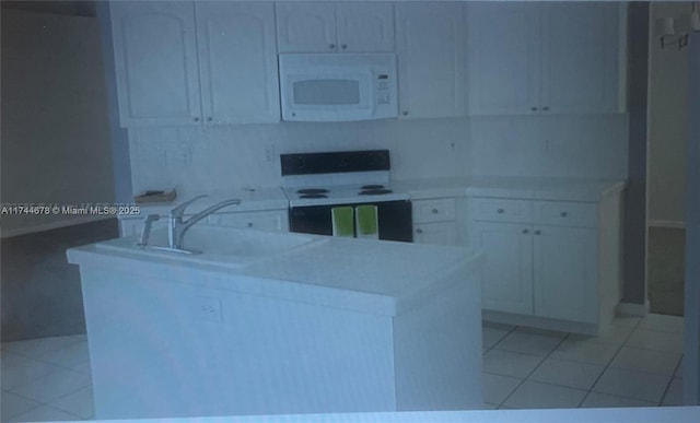 kitchen with electric stove, white microwave, light tile patterned flooring, a sink, and an island with sink