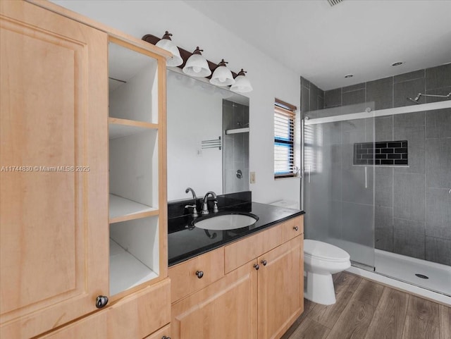 bathroom featuring wood-type flooring, toilet, a shower with shower door, and vanity