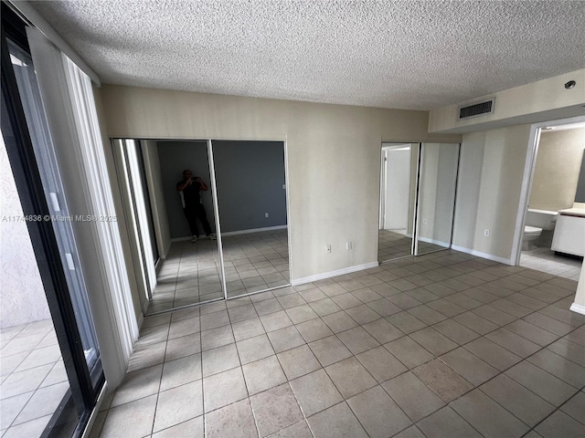 unfurnished bedroom featuring tile patterned flooring, connected bathroom, and a textured ceiling