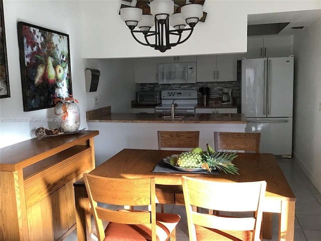 609 Waterside Dr Unit 609, Hypoluxo, FL 33462 - kitchen with white appliances, tile patterned flooring, a chandelier, decorative backsplash, and a peninsula