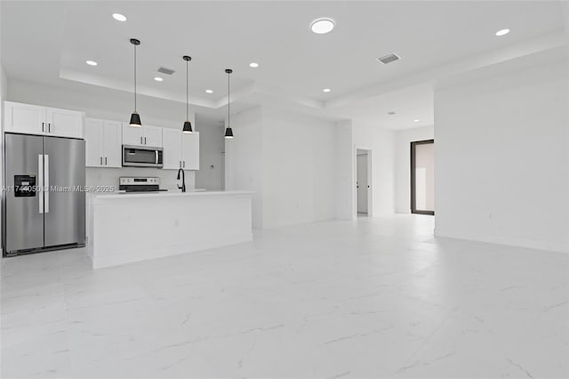 kitchen with a center island with sink, a raised ceiling, white cabinets, and appliances with stainless steel finishes