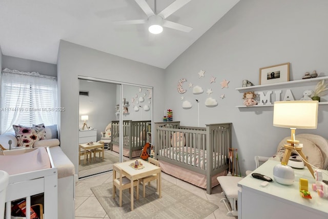 bedroom with lofted ceiling, light tile patterned floors, a crib, ceiling fan, and a closet