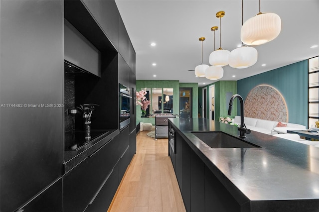 kitchen with a large island, sink, light hardwood / wood-style floors, decorative light fixtures, and stainless steel oven