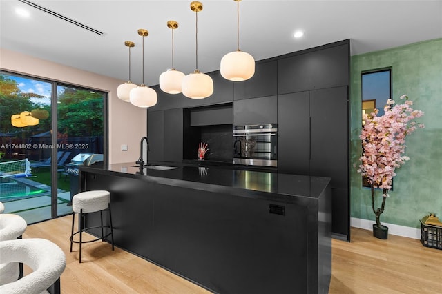 kitchen with light hardwood / wood-style floors, oven, sink, and hanging light fixtures