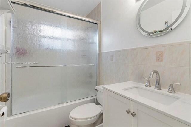 full bathroom with toilet, vanity, shower / bath combination with glass door, and tile walls