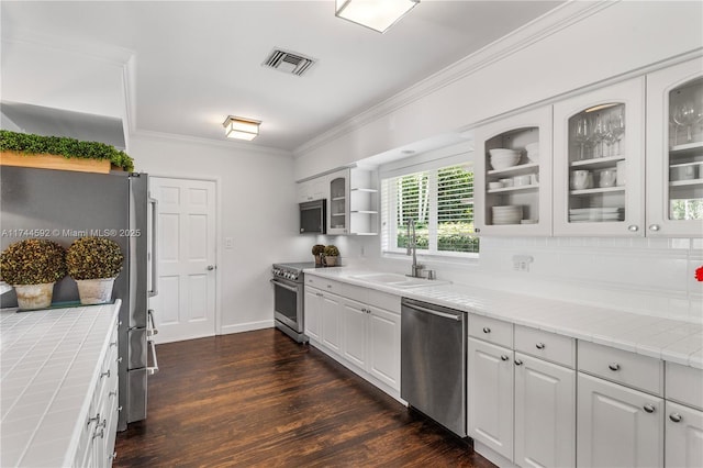 kitchen featuring tile counters, crown molding, open shelves, stainless steel appliances, and a sink
