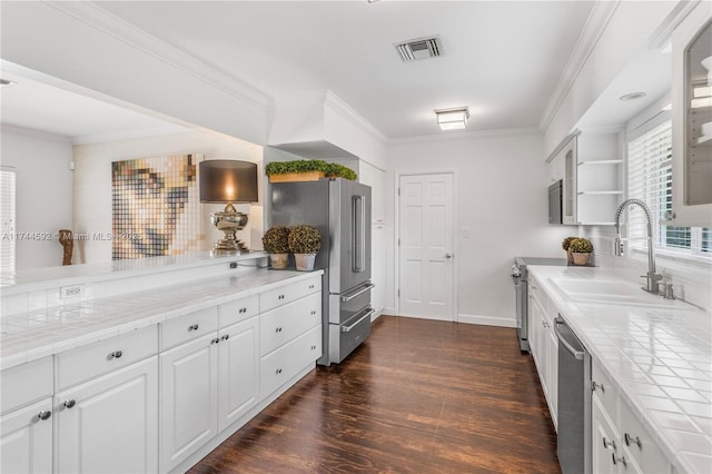 kitchen featuring a sink, tile counters, appliances with stainless steel finishes, dark wood-style floors, and visible vents