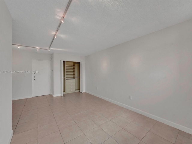 empty room featuring light tile patterned flooring, rail lighting, and a textured ceiling