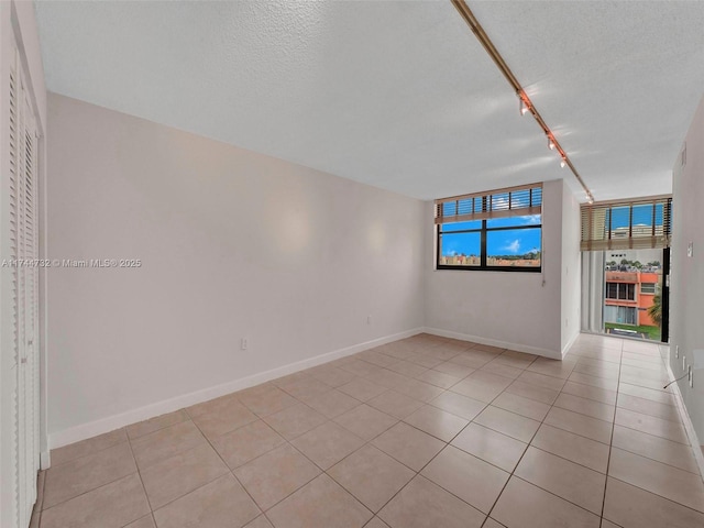 unfurnished room with rail lighting, light tile patterned flooring, and a textured ceiling