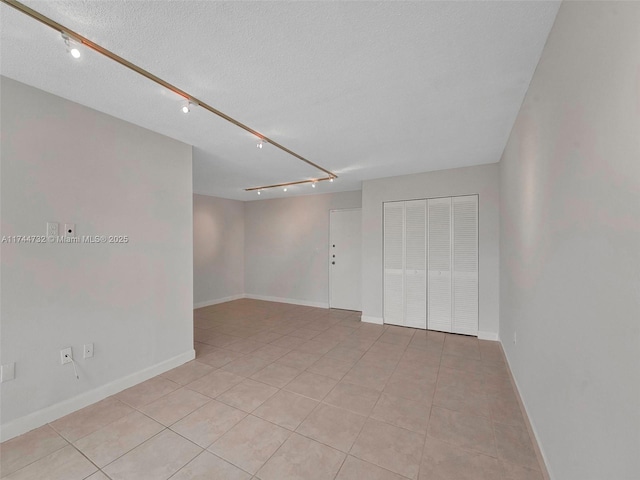 tiled empty room featuring rail lighting and a textured ceiling