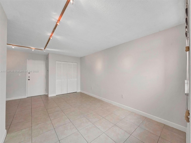 unfurnished bedroom featuring light tile patterned floors, rail lighting, a closet, and a textured ceiling