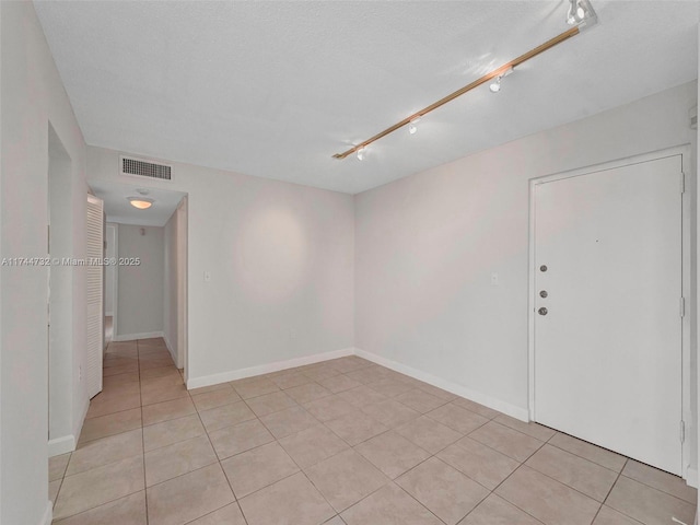 tiled empty room with track lighting and a textured ceiling