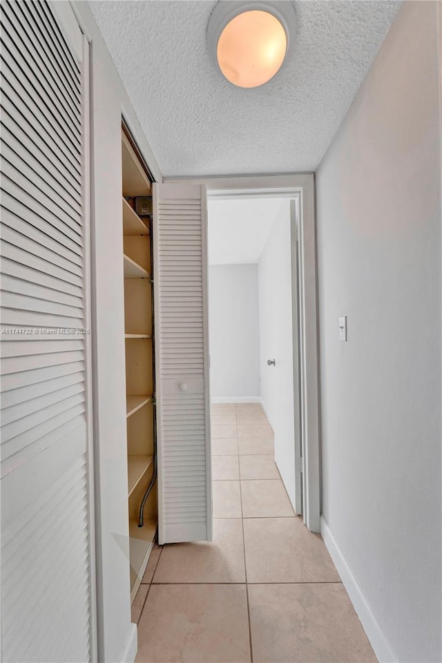 hallway with a textured ceiling and light tile patterned floors