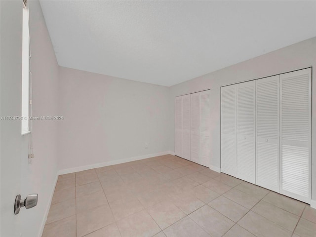 unfurnished bedroom featuring light tile patterned floors and two closets