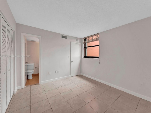 unfurnished bedroom with light tile patterned floors, ensuite bath, a closet, and a textured ceiling