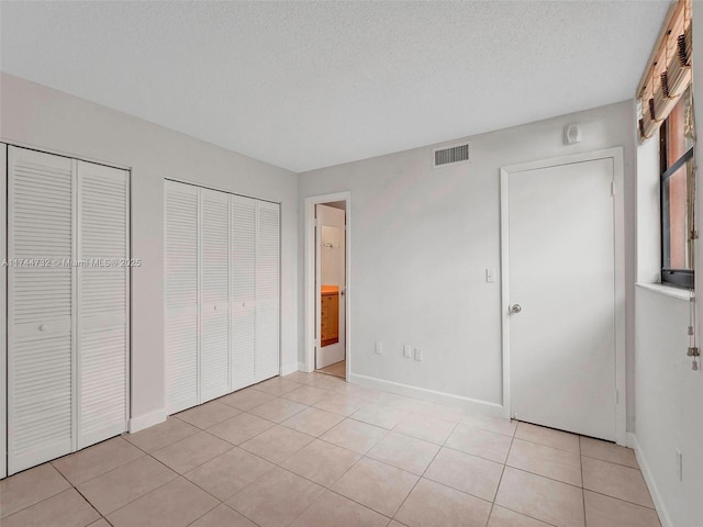 unfurnished bedroom featuring multiple closets, light tile patterned flooring, and a textured ceiling