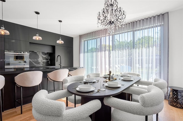 dining room with sink, a chandelier, a healthy amount of sunlight, and light wood-type flooring