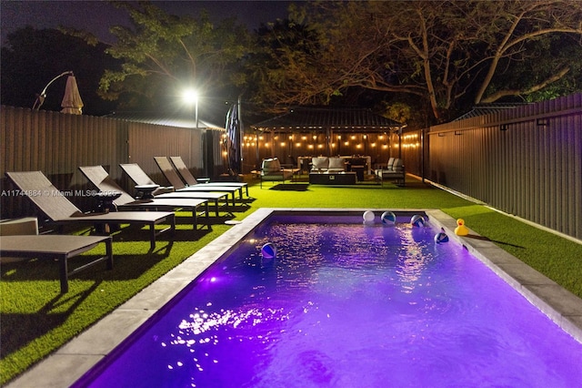 pool at night featuring an outdoor hangout area, pool water feature, and a lawn