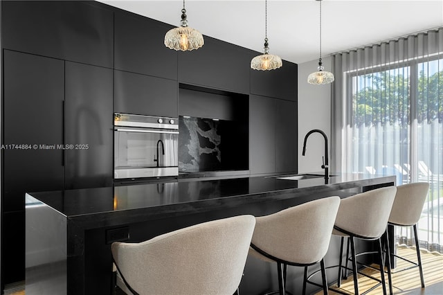 kitchen featuring hanging light fixtures, a kitchen island with sink, sink, and wall oven