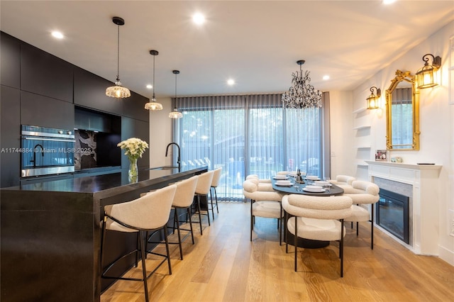 kitchen featuring pendant lighting, sink, oven, a large island with sink, and light wood-type flooring