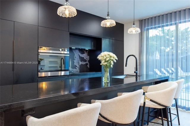 kitchen featuring stainless steel oven, a kitchen bar, sink, and hanging light fixtures