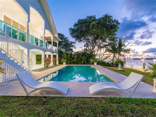 pool at dusk featuring a patio and a water view